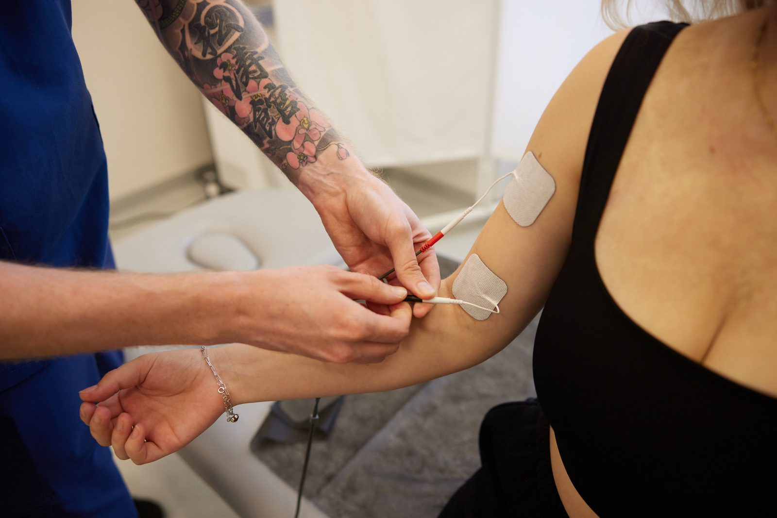 Fizjoterapeuta mocuje elektrody do elektroterapii na kończynie górnej pacjentki